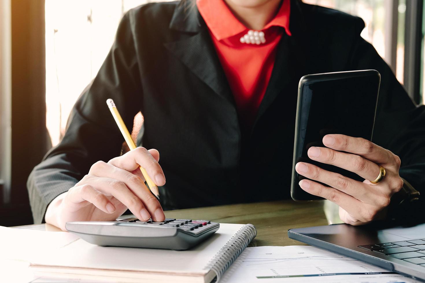 Businesswoman looking at smartphone and using calculator photo