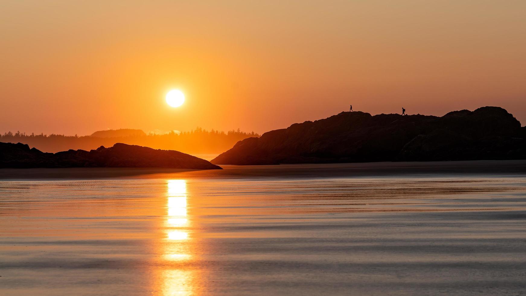 Silhouettes of people walking on rocky coast photo