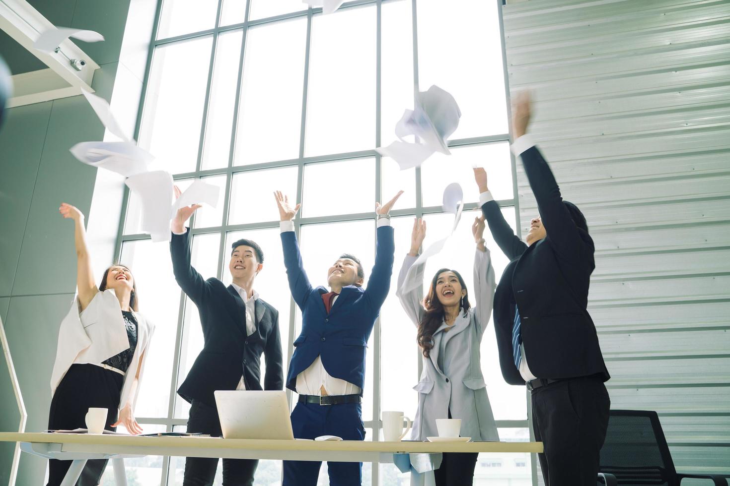 empresarios emocionados sonrisa feliz, grupo de empresarios confía en tirar papel en el aire mientras trabajaba detrás de la pared de cristal, concepto de equipo de éxito. foto