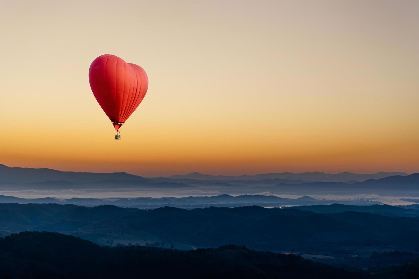 Red hot air balloon in the shape of a heart flying over the mountain photo