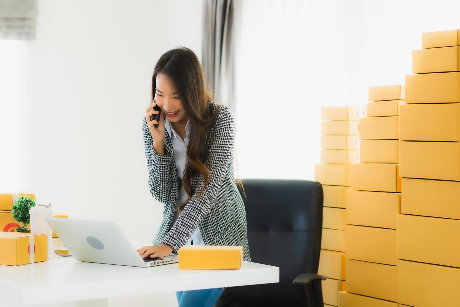 Businesswoman making a call and working on computer with packages behind her photo