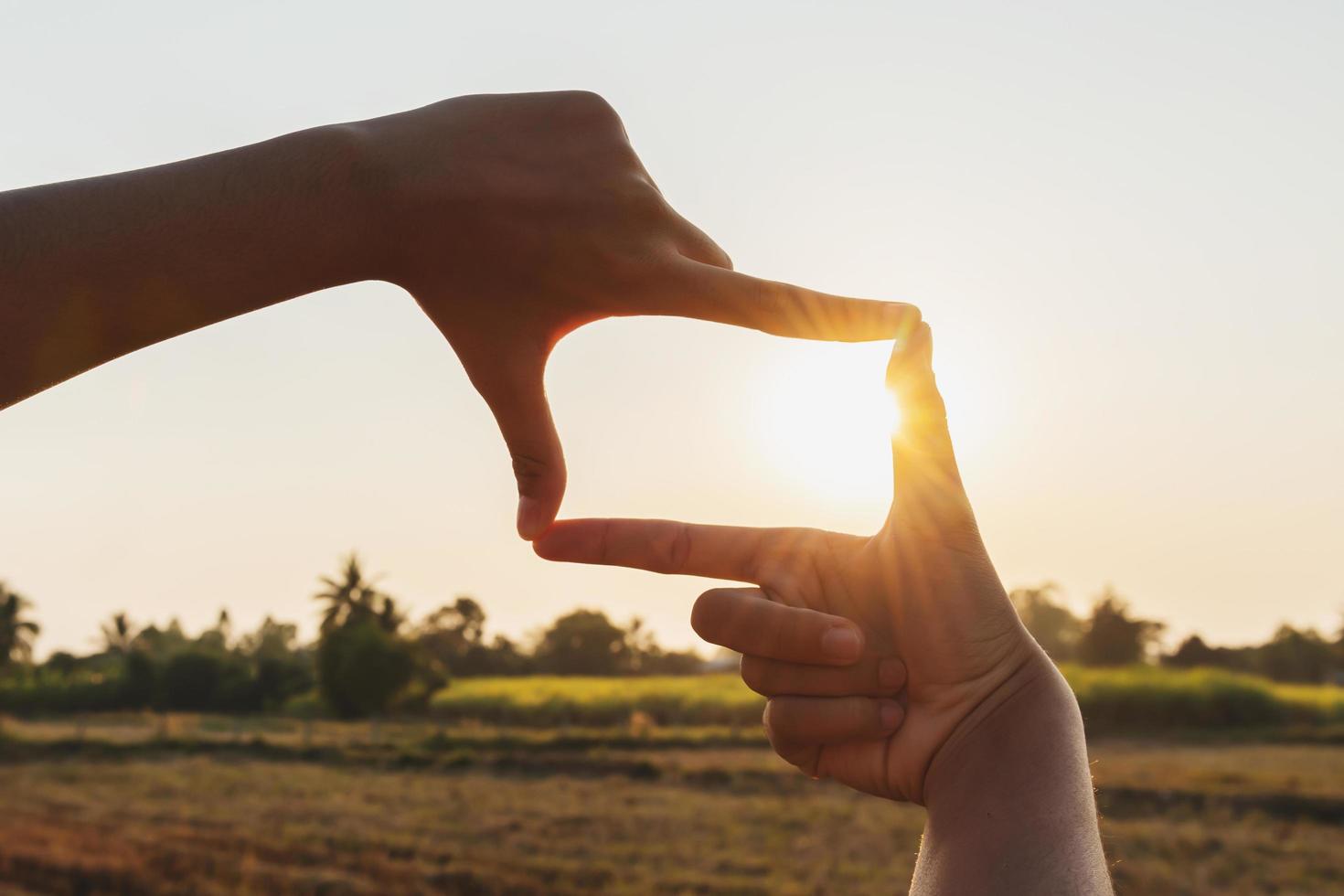 primer plano de una mano enmarcando la puesta de sol foto