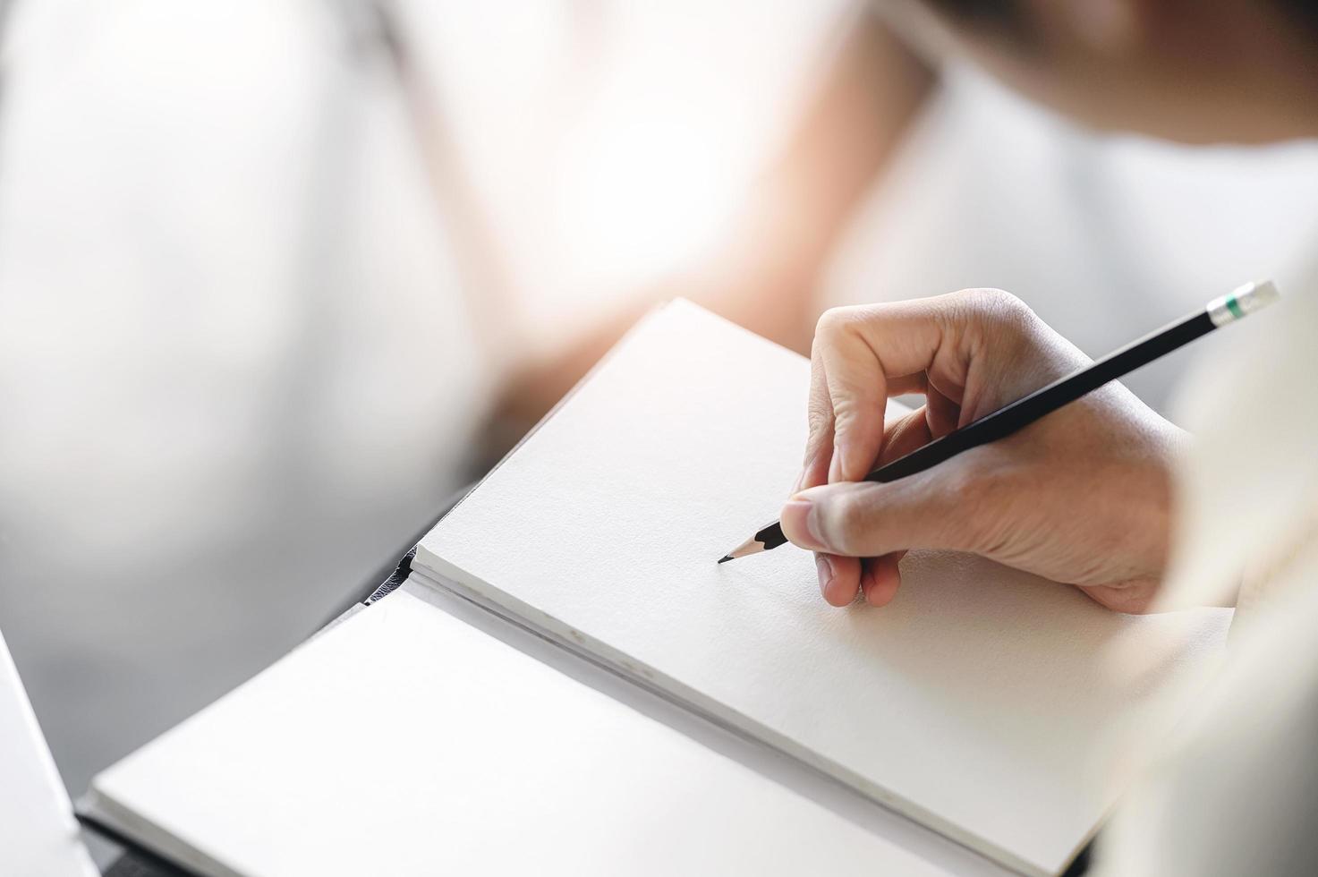 Man hand writes on notebook with pencil photo