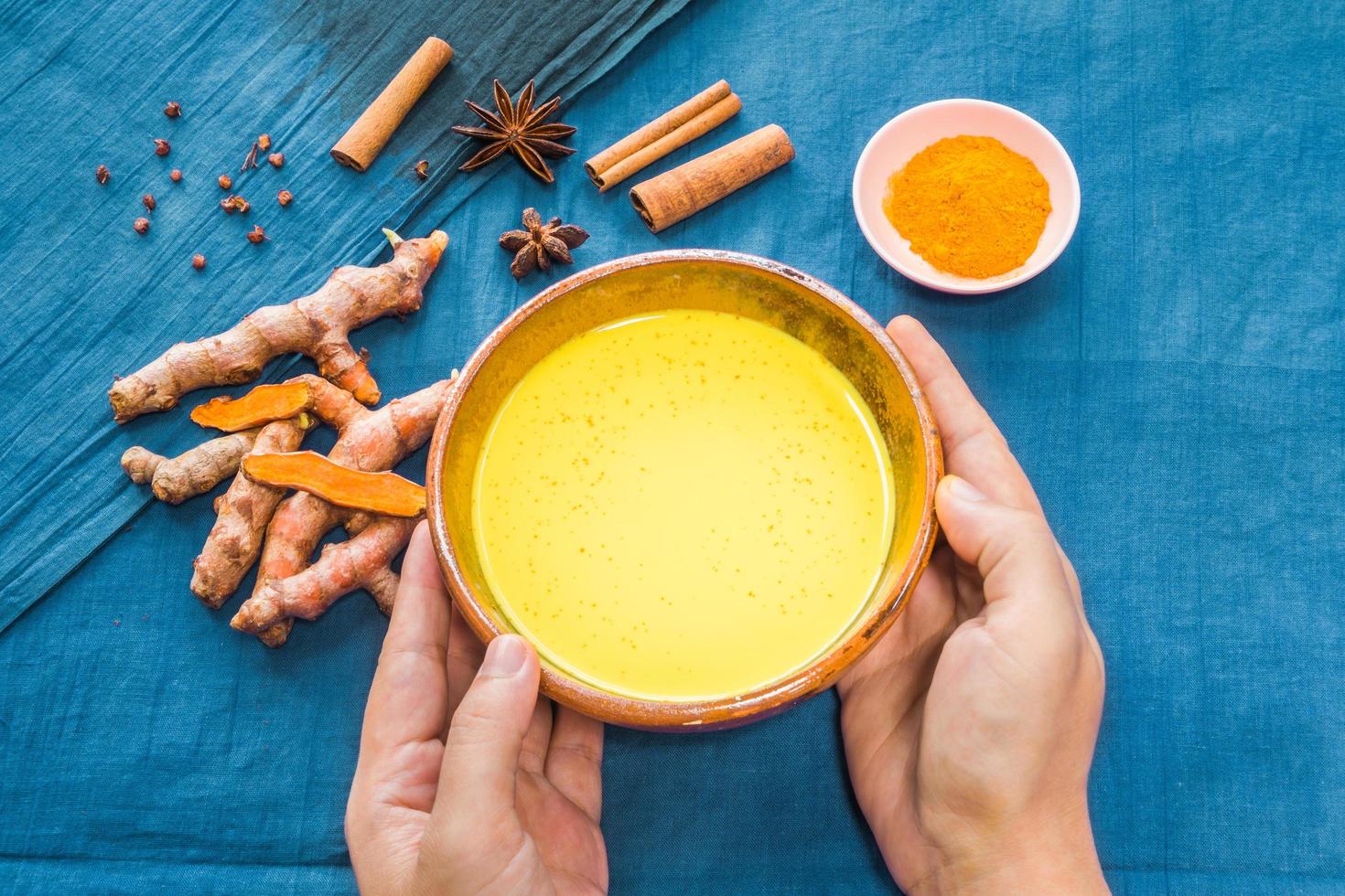 Manos sosteniendo leche dorada o café con leche de cúrcuma con ingredientes foto