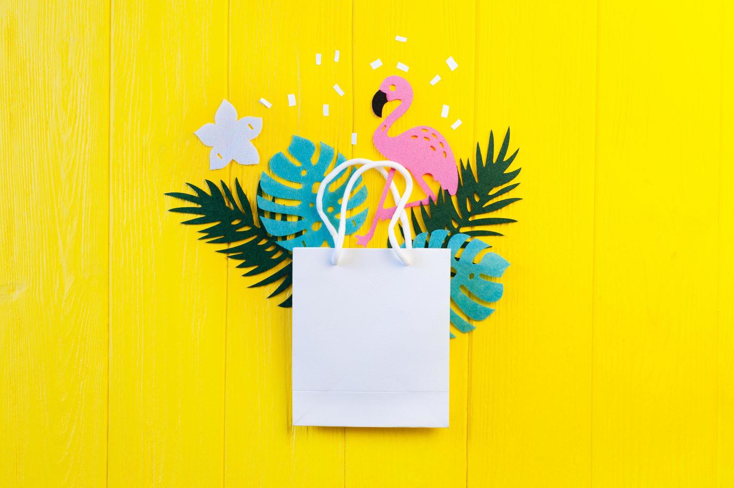 Mockup of blank paper with leaves and flamingo on yellow wooden background photo