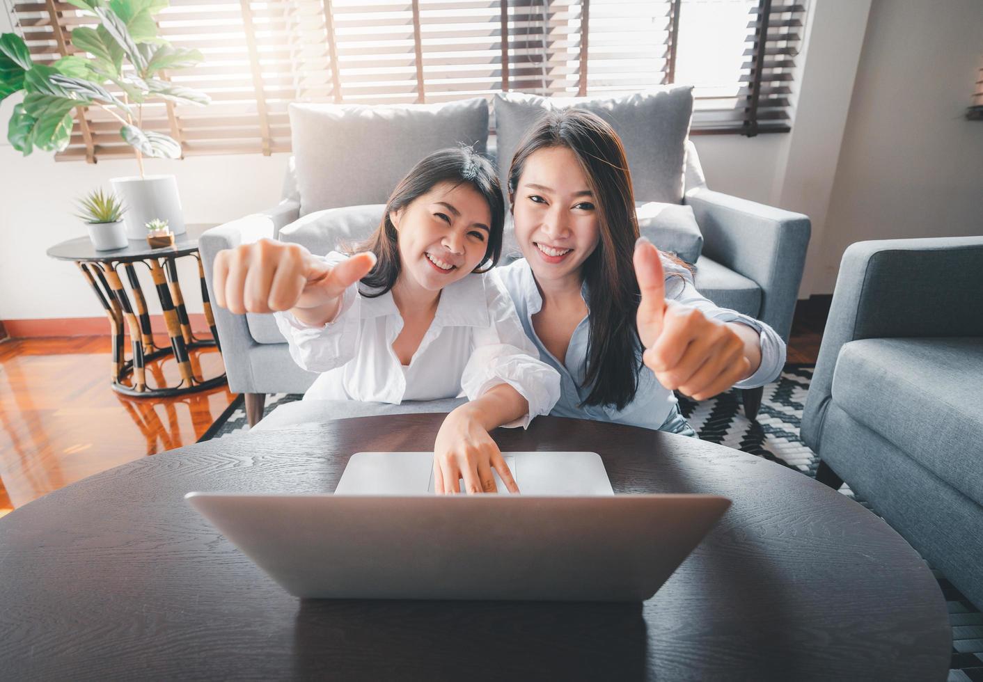 Asian women friends using laptop giving thumbs up gesture photo