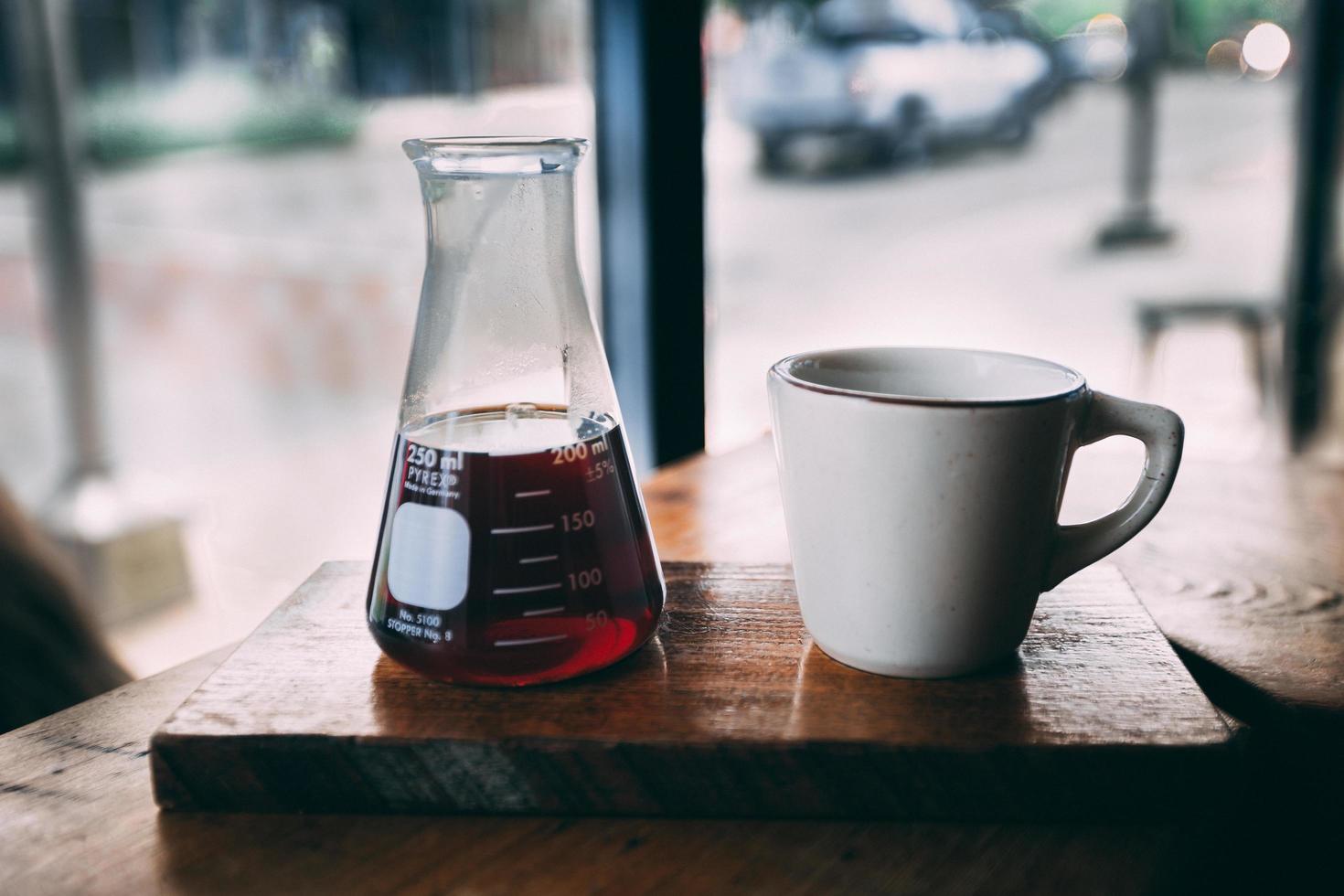 Erlenmeyer flask and white mug on brown wooden table photo