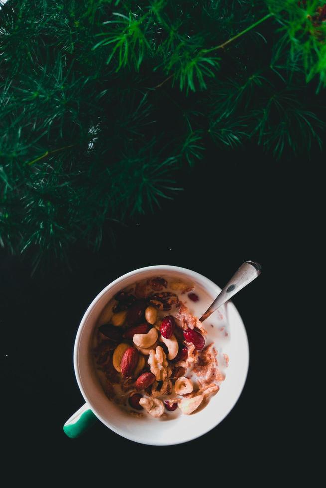 cereal, nueces, leche y cuchara en una taza junto a la planta foto