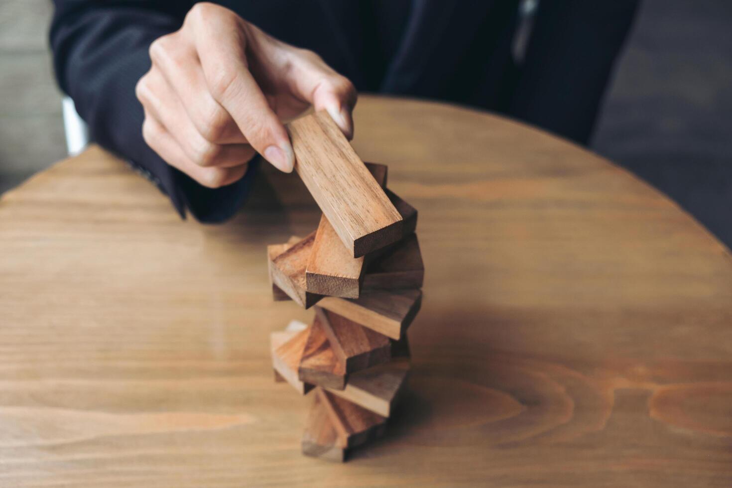 Mano del empresario colocando y tirando de un bloque de madera en la torre foto