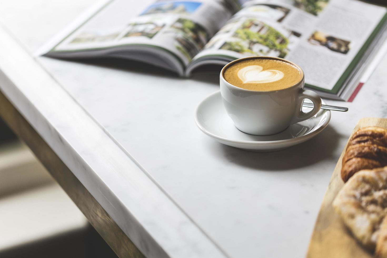 Taza de café de cerámica blanca con platillo sobre mesa blanca foto