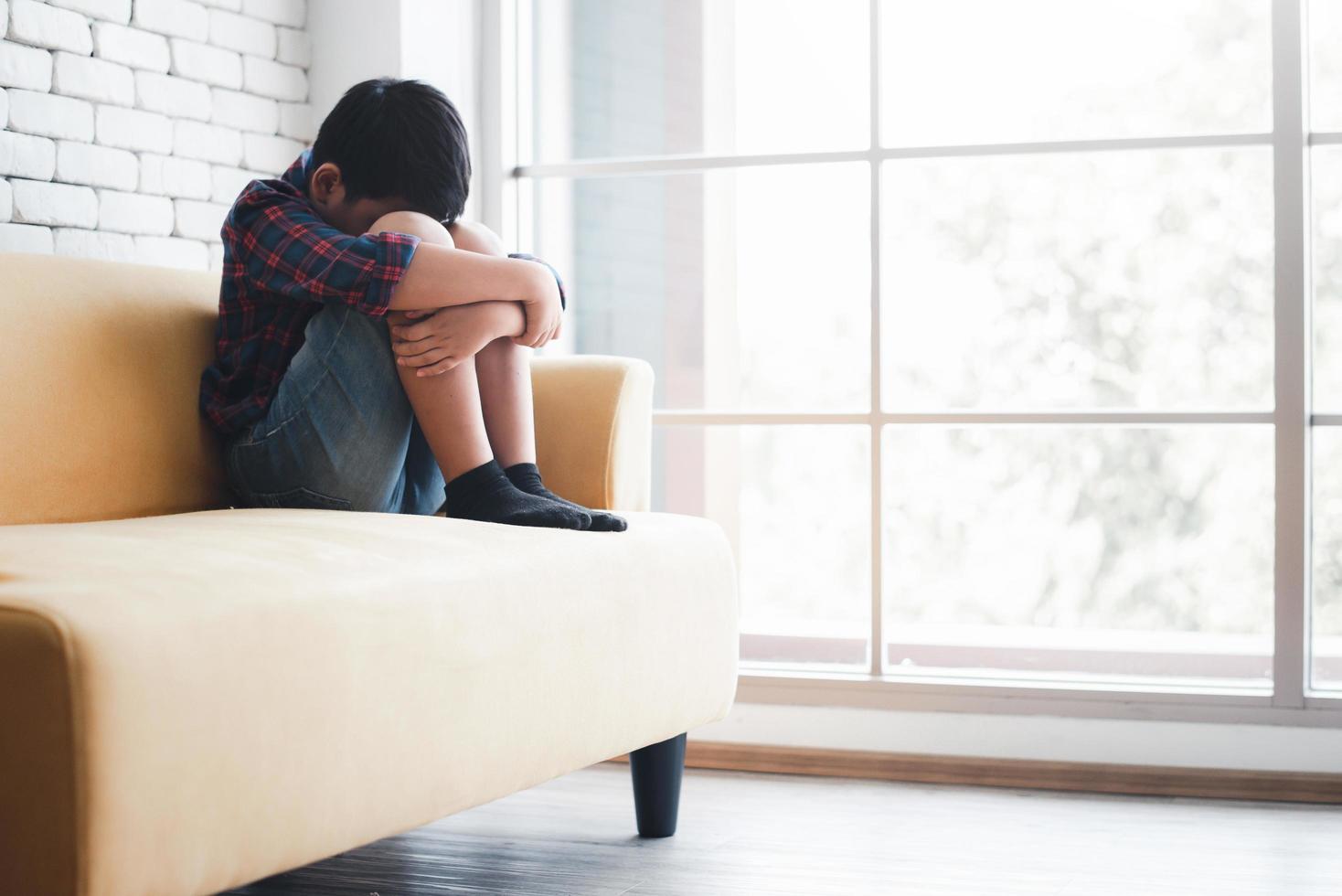 Asian boy sitting alone on sofa feeling sad photo