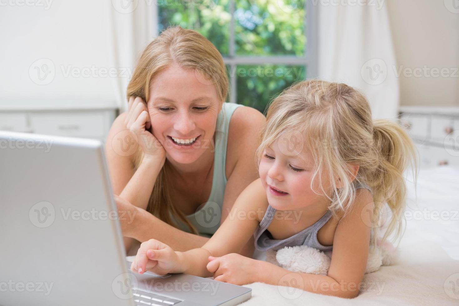 Cute little girl and mother on bed using laptop photo