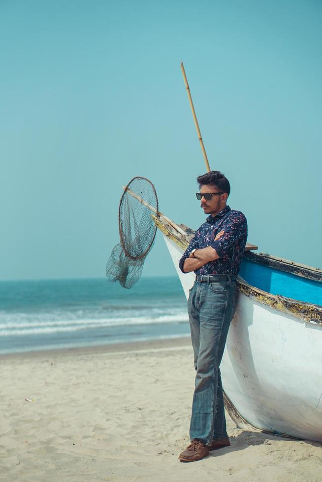 Young man standing with a boat near beach photo