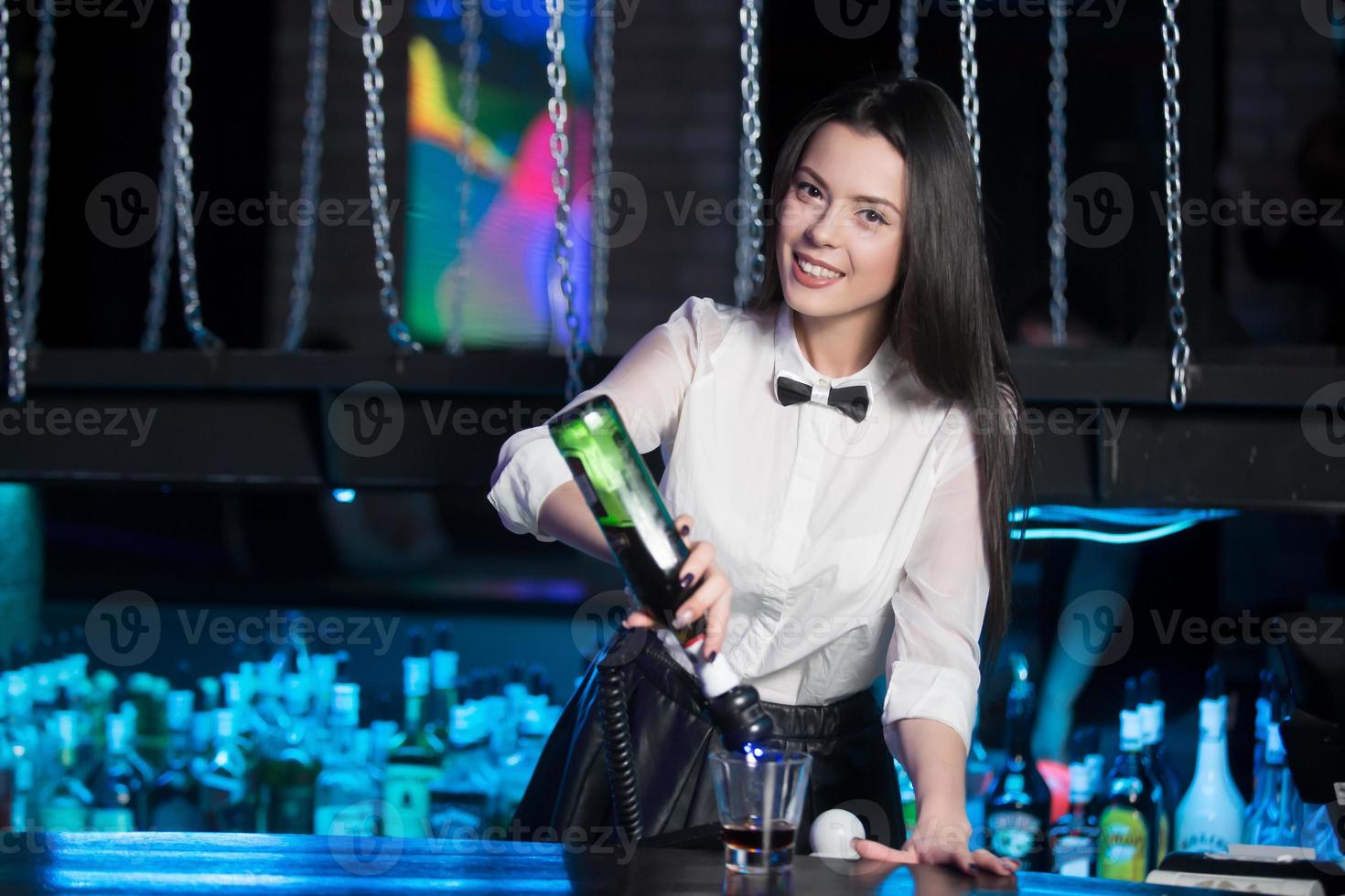 Smiling brunette bartender pouring martini photo