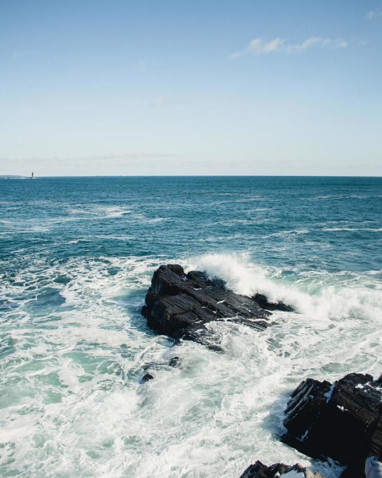 Olas del océano rompiendo en las rocas bajo un cielo azul foto