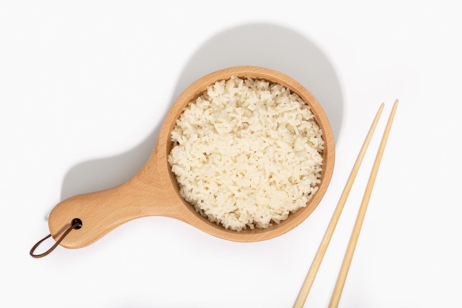 Cooked rice in wooden spoon and chopsticks on white background photo