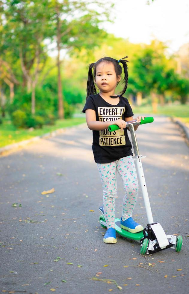 niña aprendiendo a andar en scooter en un parque foto