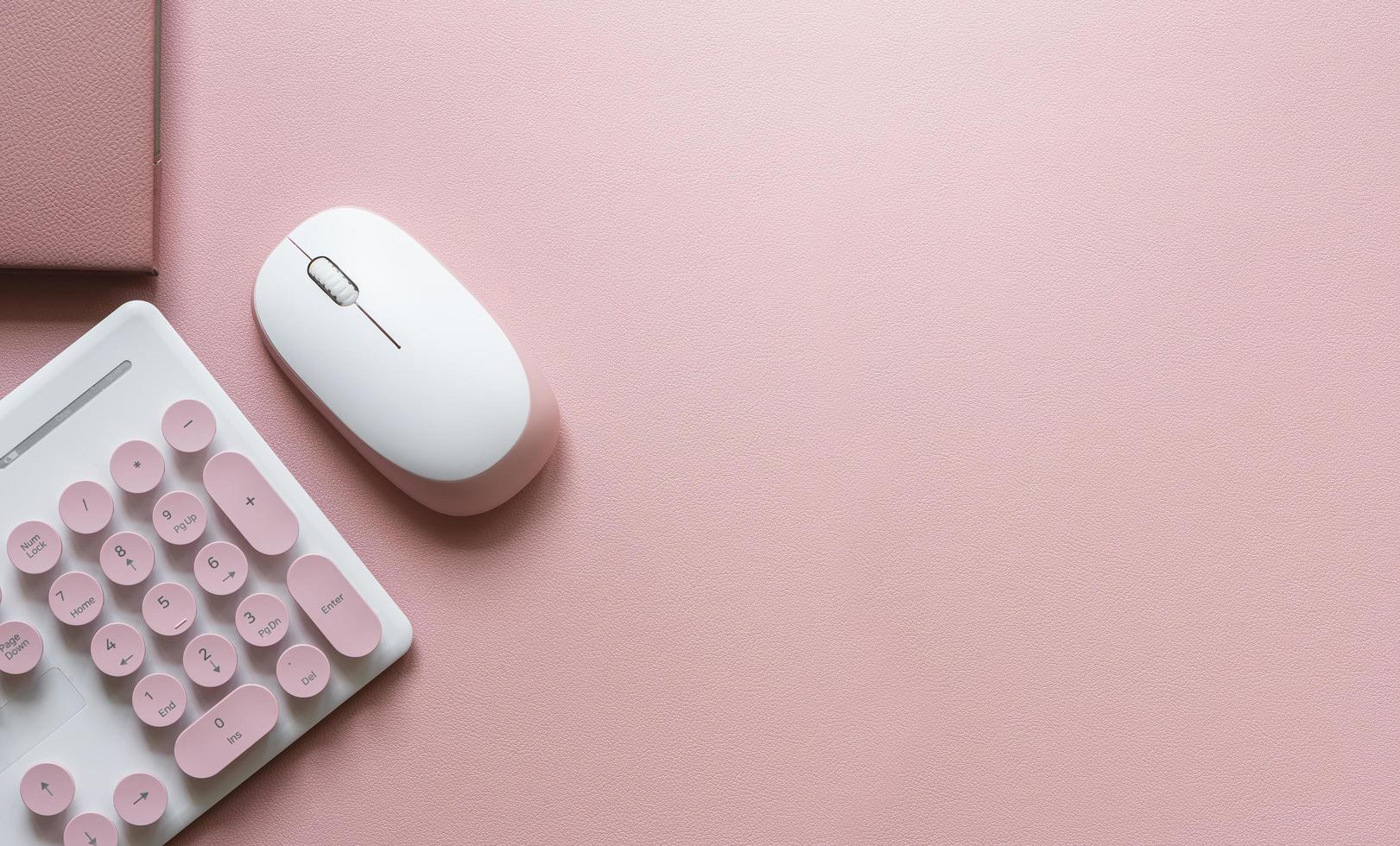 Top view of a pink workspace with a keyboard, mouse and book photo