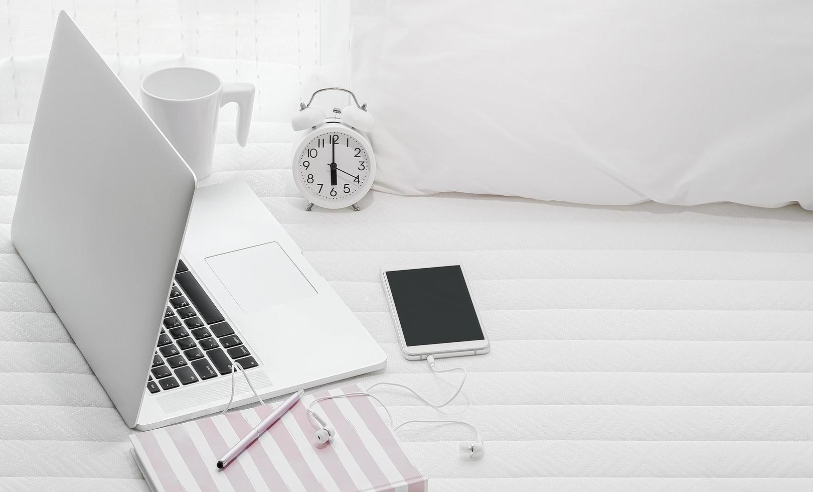 Laptop with clock, phone and coffee on a bed photo