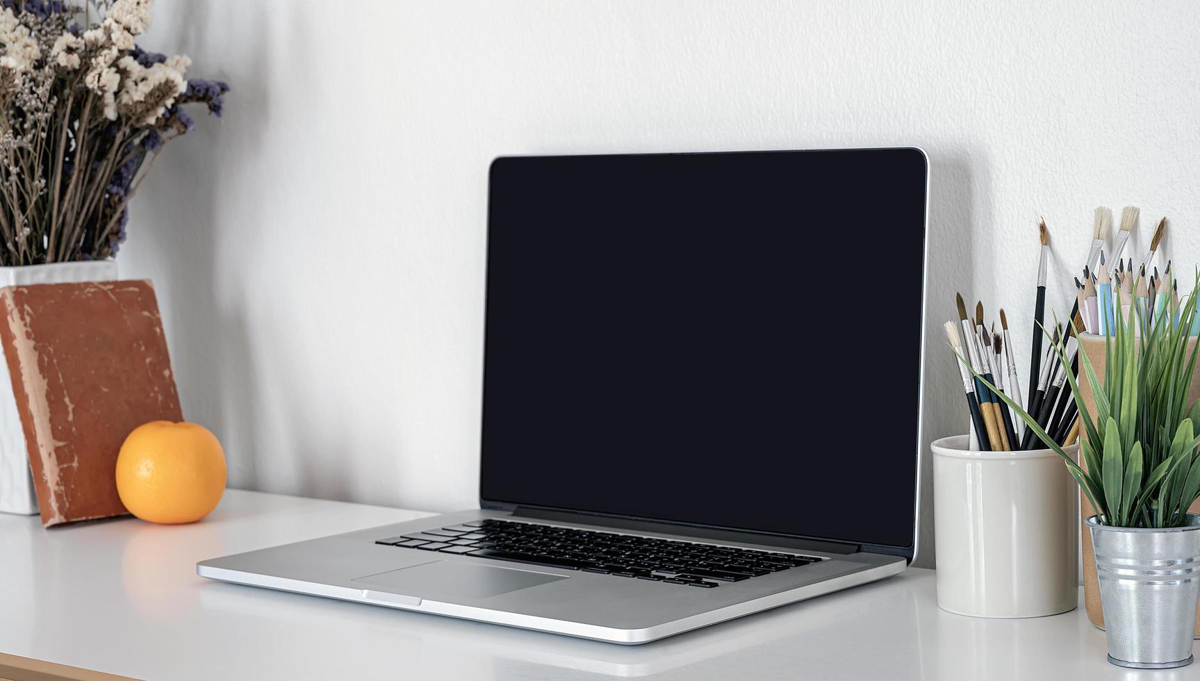 Laptop with brushes in cups on a desk photo