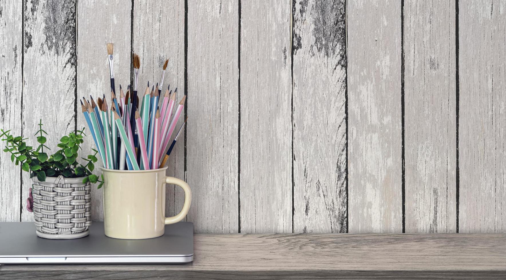 Cup of pencils and houseplant on laptop on wooden table photo