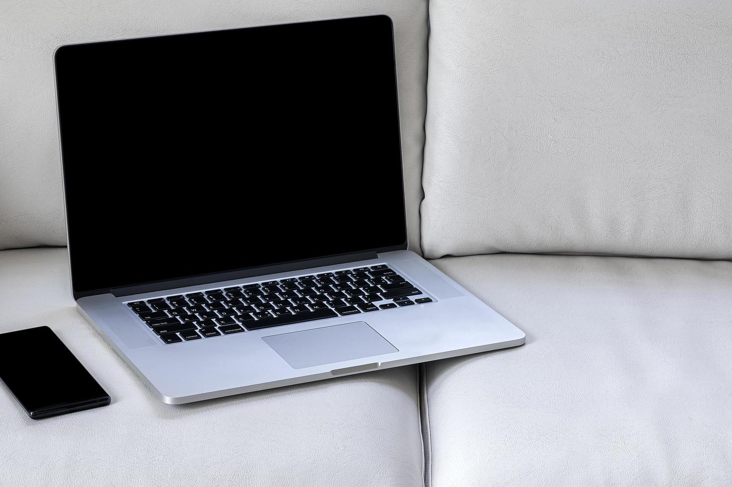 Laptop mockup with a smartphone on a sofa photo