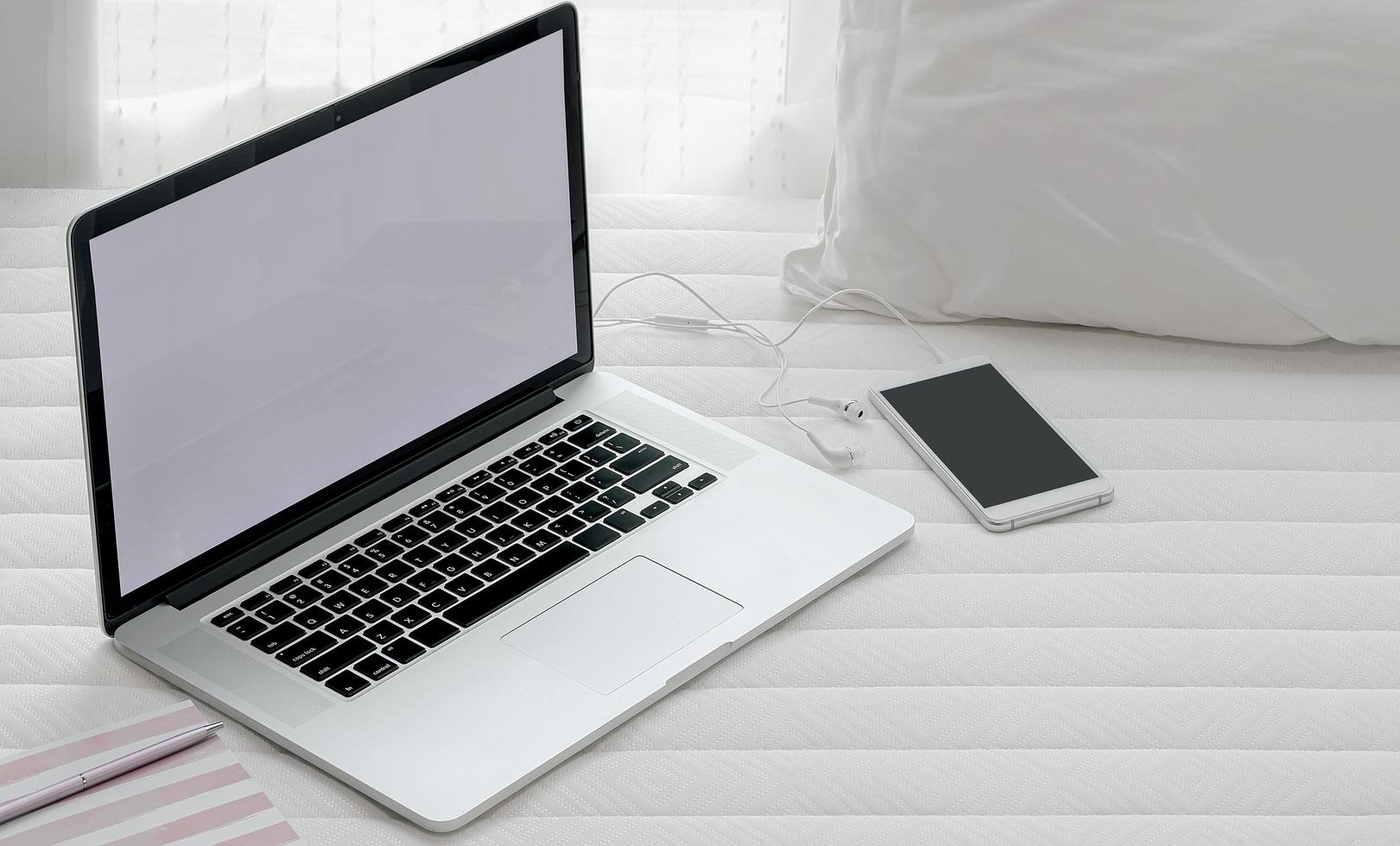 Laptop and smartphone on bed mockup photo