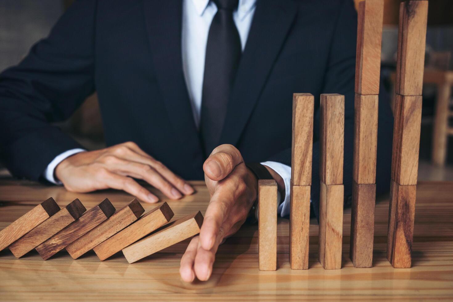 Close-up of a businessman stopping wooden block from falling photo