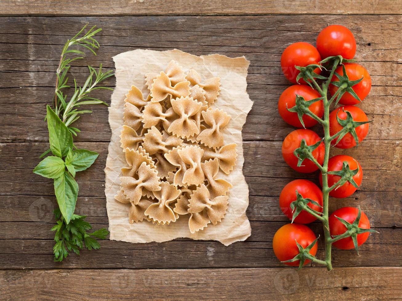 Pasta, tomatoes and herbs on wooden background photo