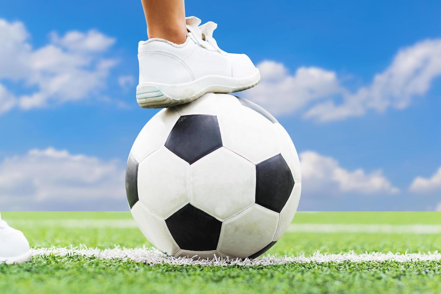 pies de un niño con zapatillas blancas pisando un balón de fútbol. foto