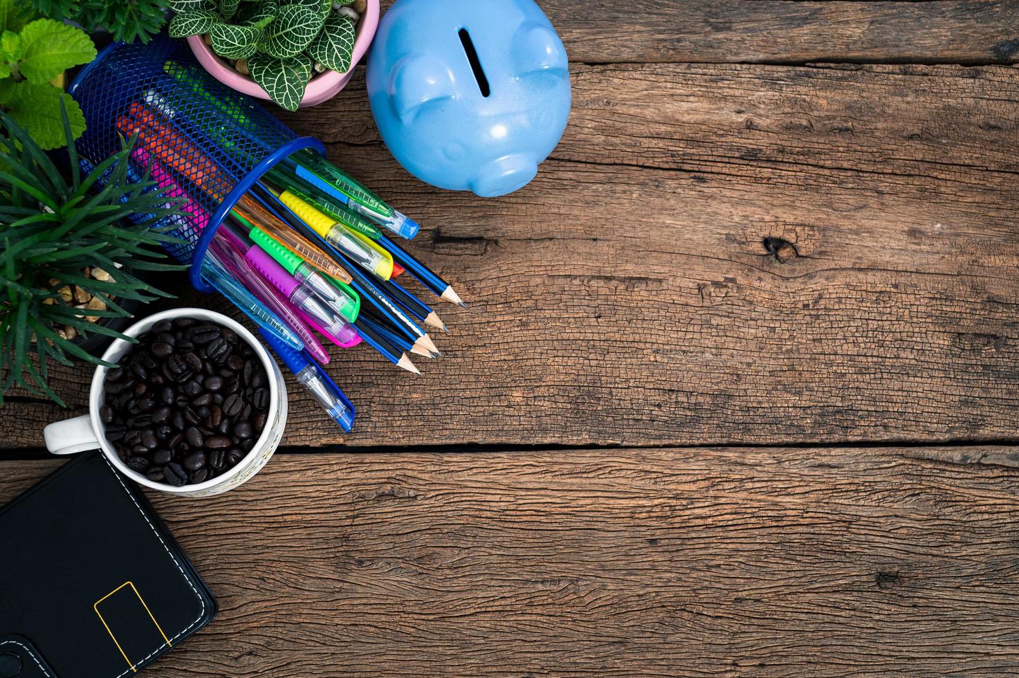 Piggy bank, plants, coffee, notebook, pens and pencils on the desk photo