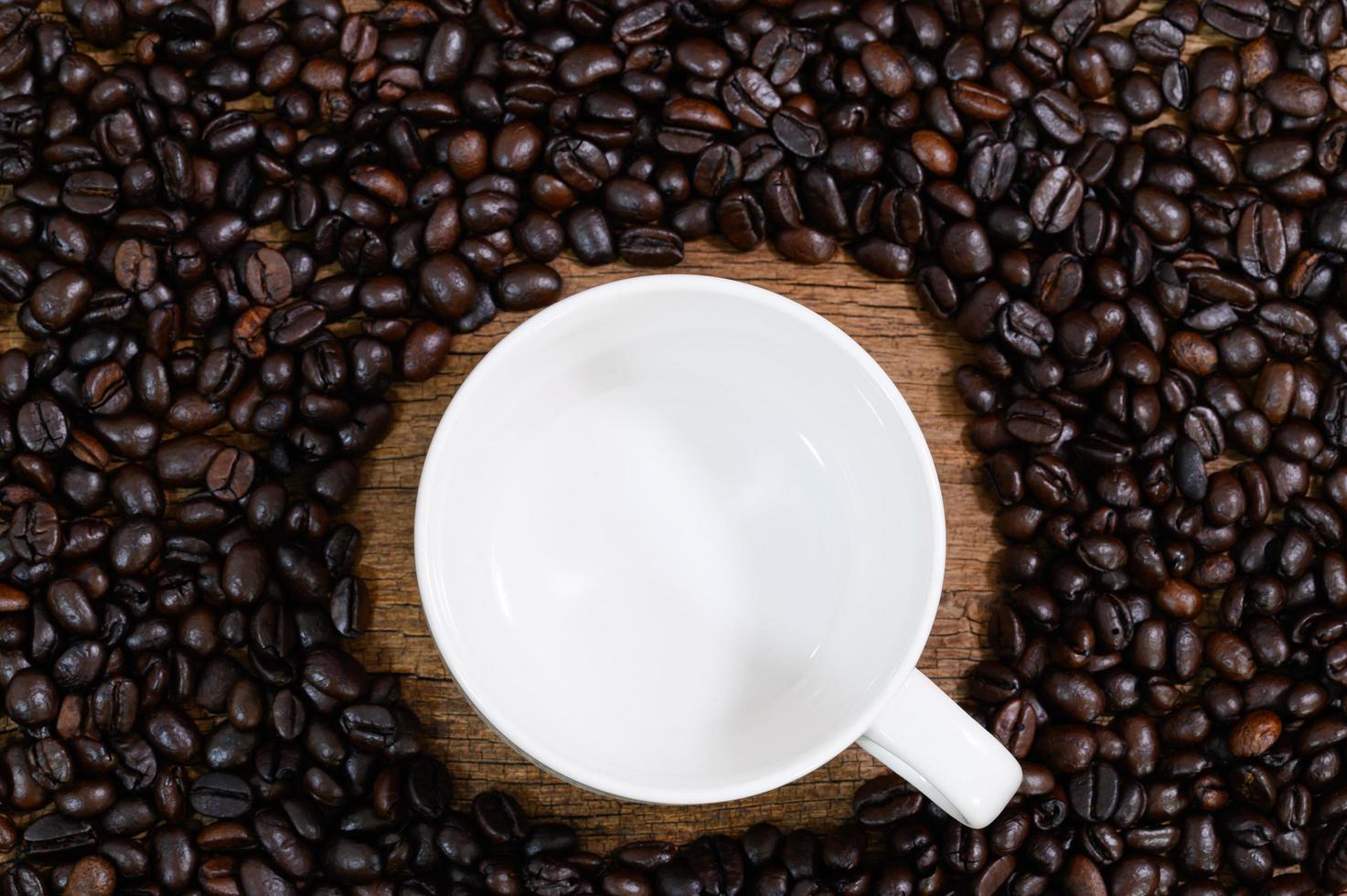 taza vacía colocada sobre la mesa con granos de café alrededor foto