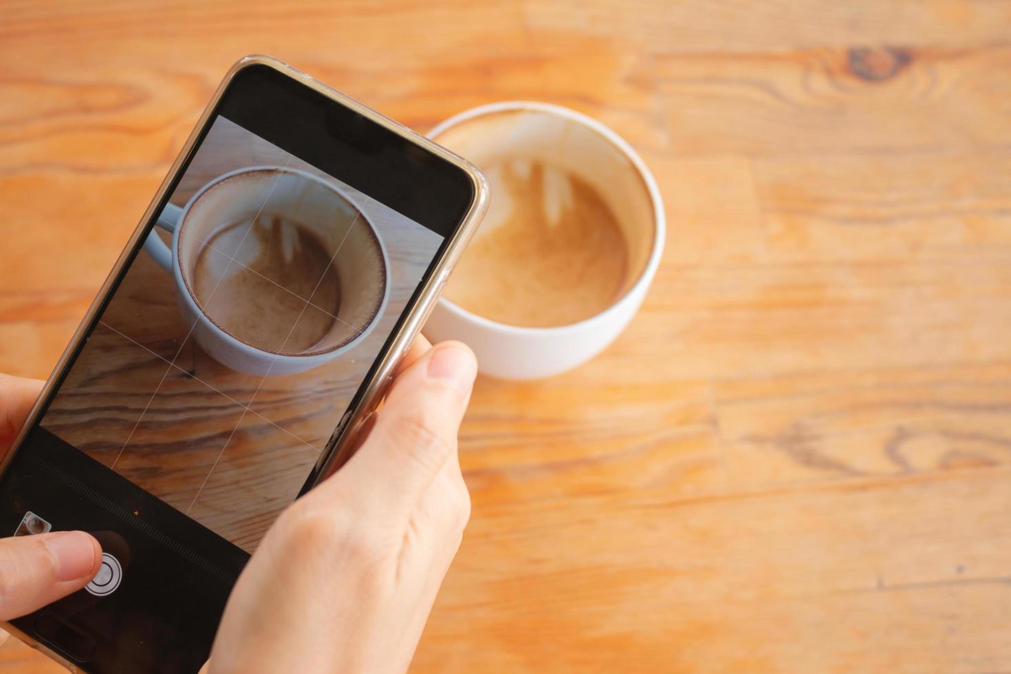 A woman uses cellphone to take a photo of a cup of hot coffee