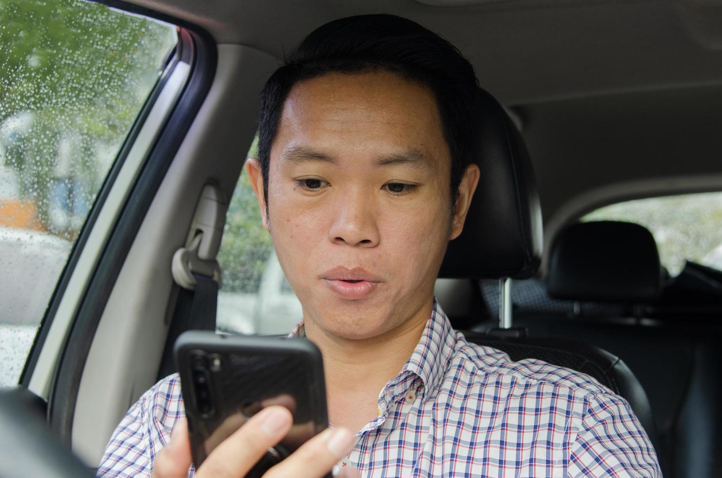 hombre asiático, mirar teléfono inteligente, en el coche foto