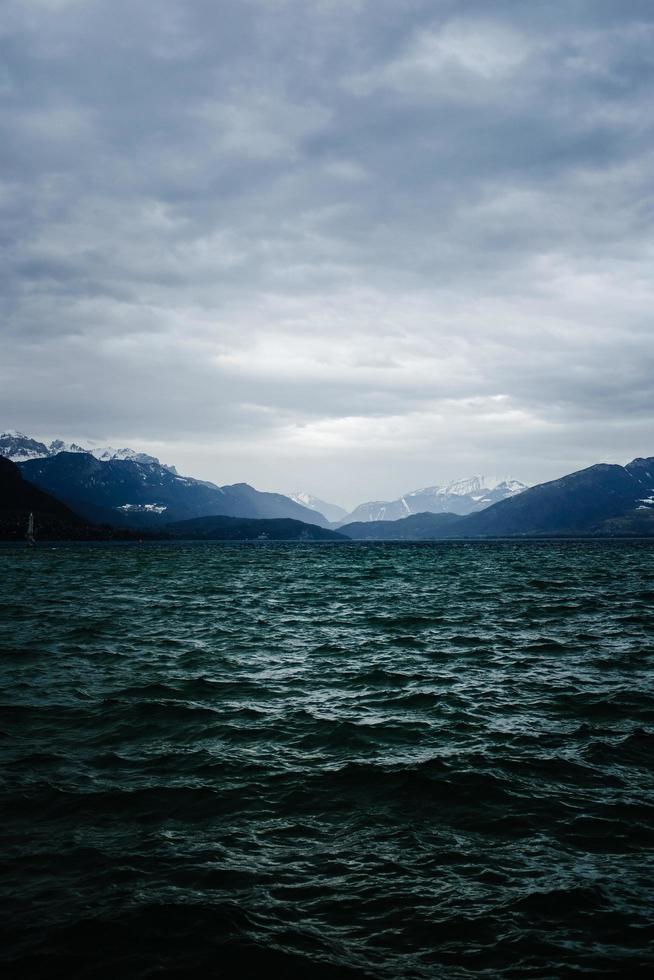 Body of water near mountain under cloudy sky photo