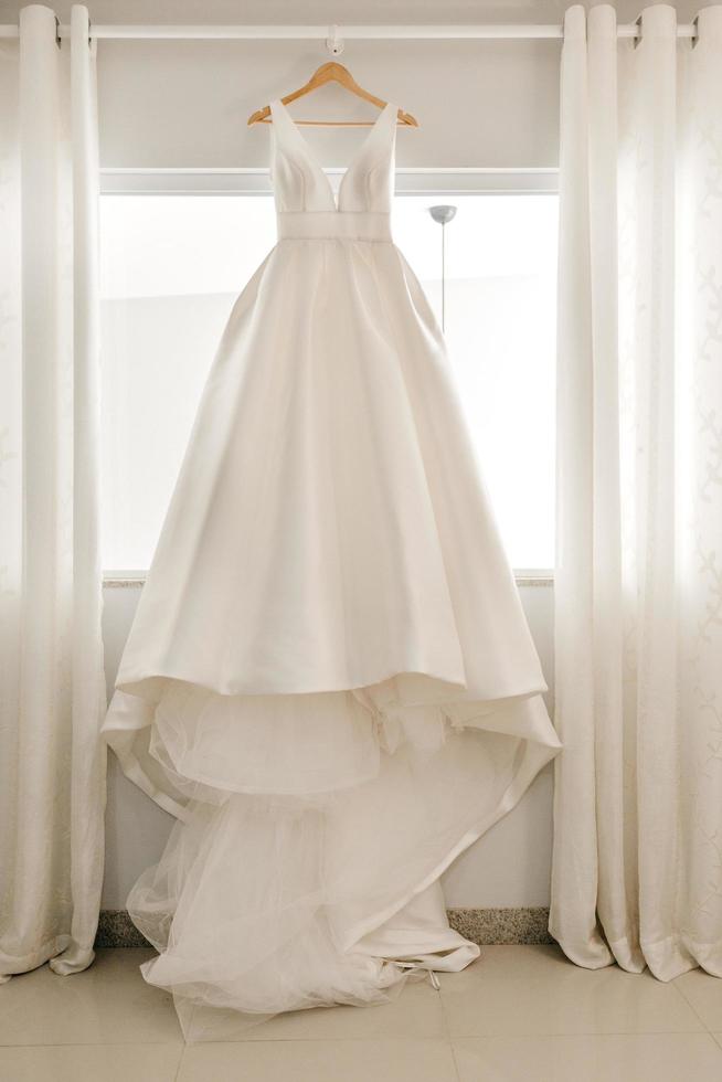 White wedding dress on hanger near window photo