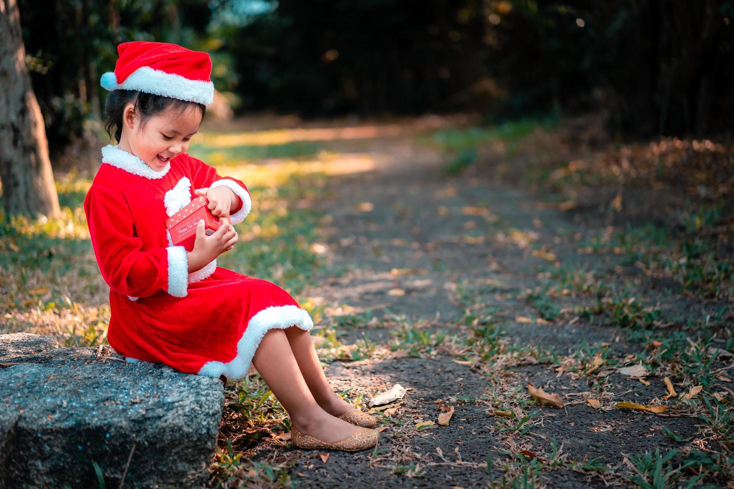 niña asiática en traje rojo de santa claus con caja presente foto