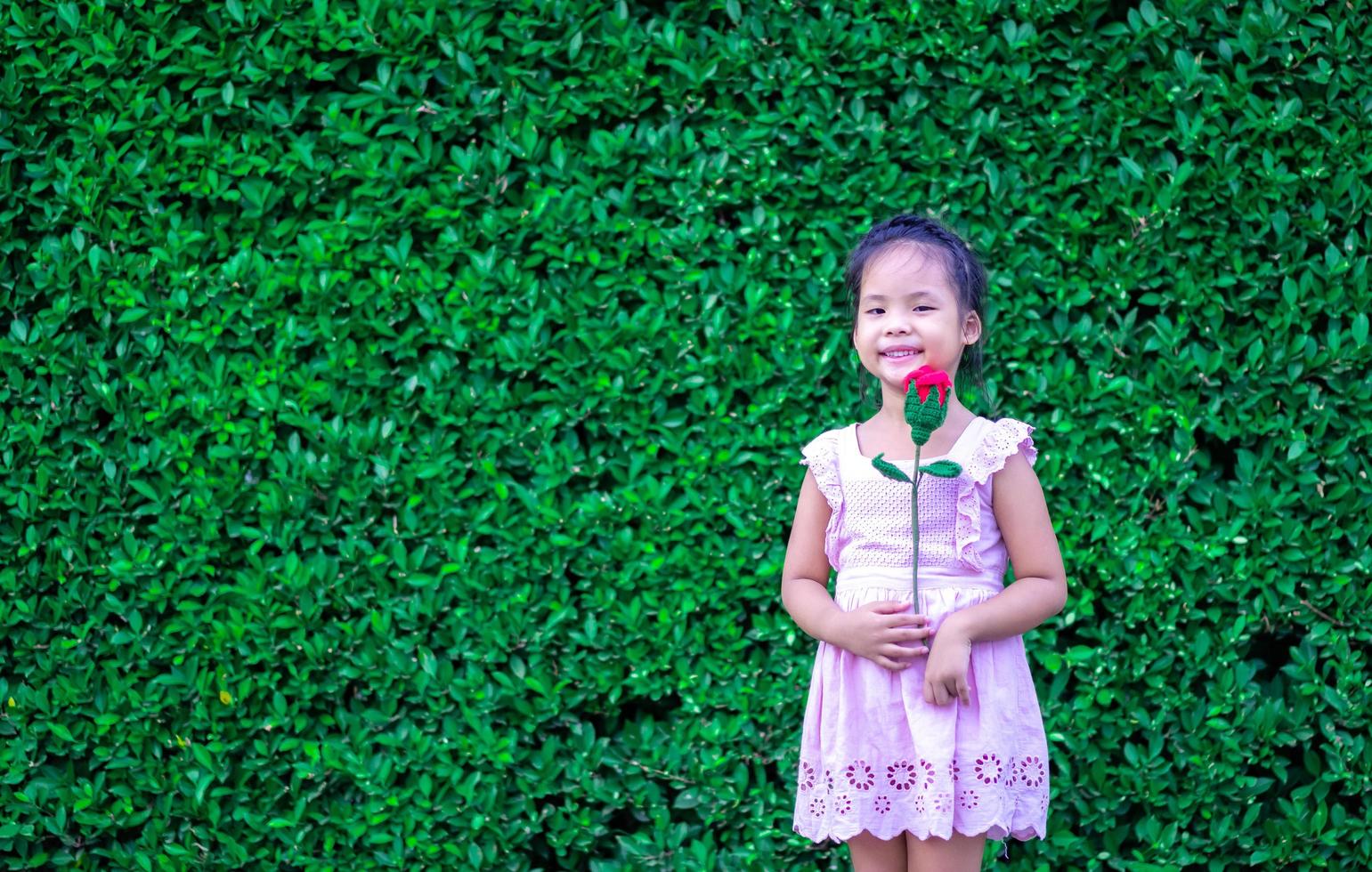 linda niña asiática en vestido sosteniendo una rosa roja en el parque foto