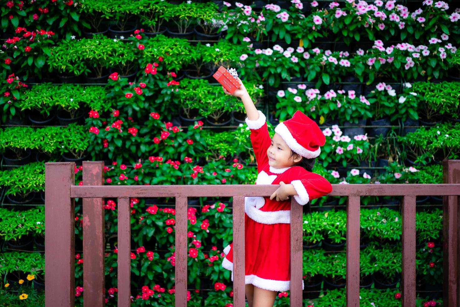 Little Asian girl in red Santa Claus costume with present box in the park photo