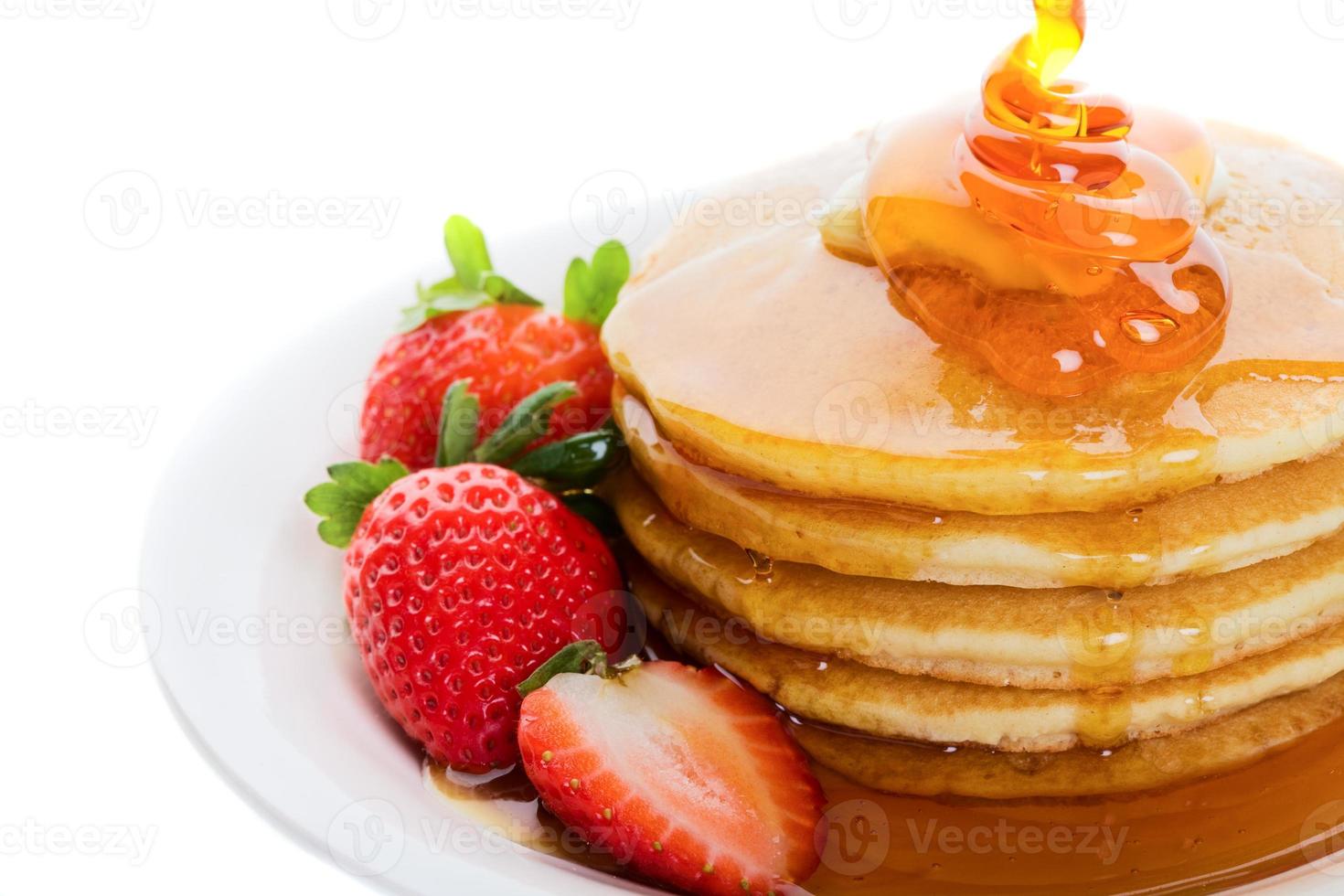 Five pancakes covered in syrup served with strawberries photo