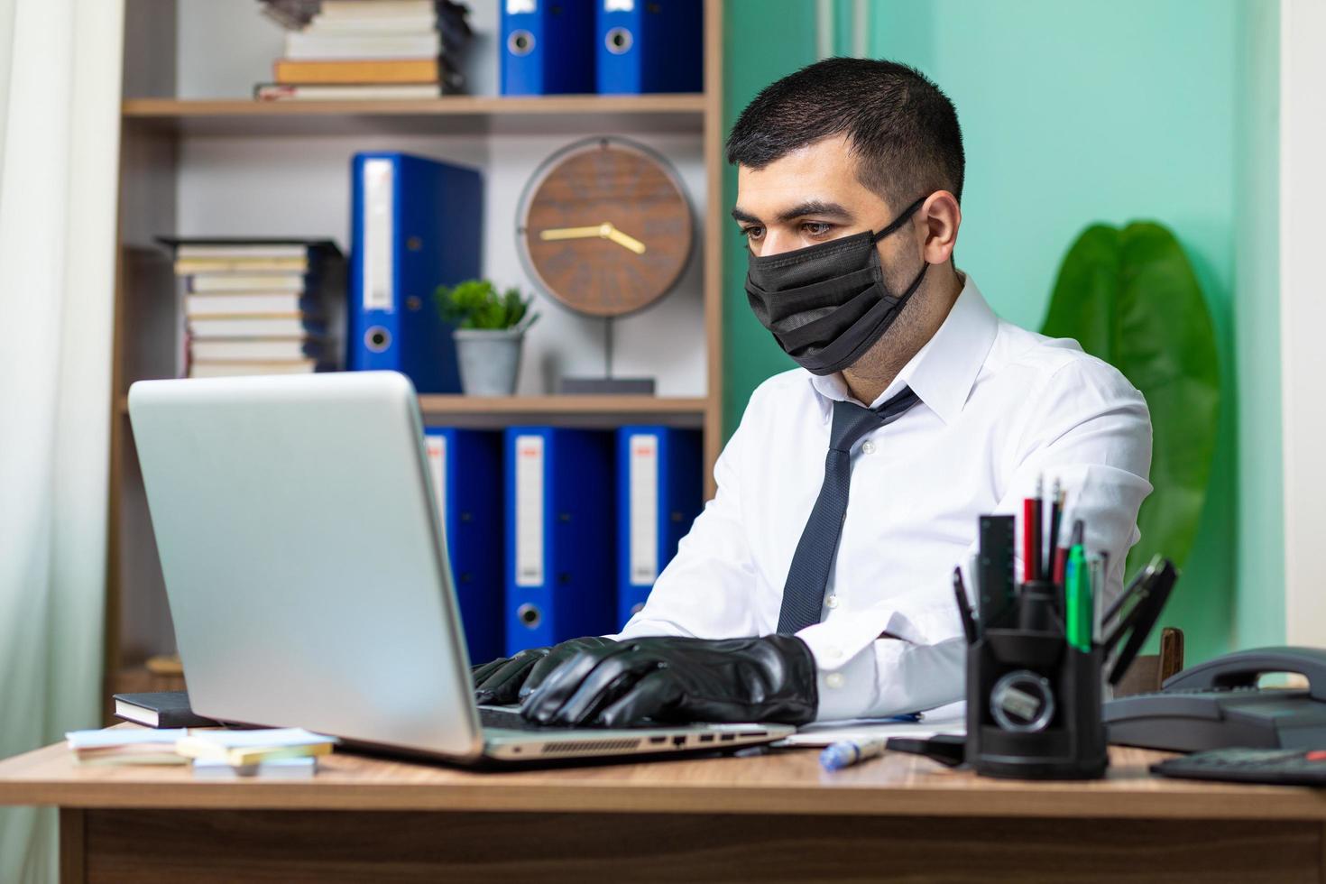 Hombre de negocios joven que trabaja en la computadora portátil con máscara protectora médica negra foto