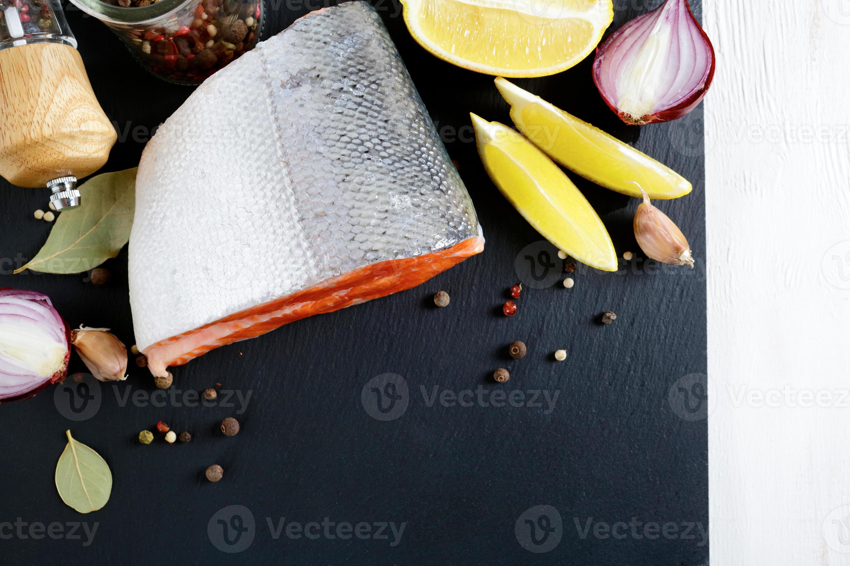Filete de salmón crudo sobre pizarra con limón y especias foto