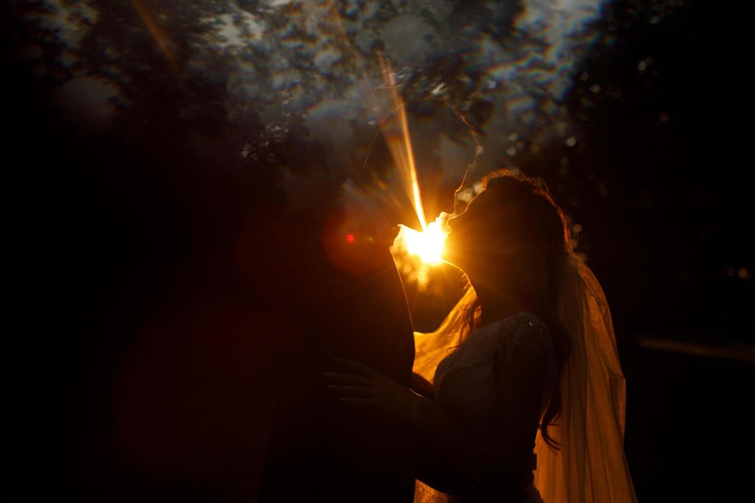 la luz del atardecer brilla detrás de la pareja de novios besándose en el parque foto