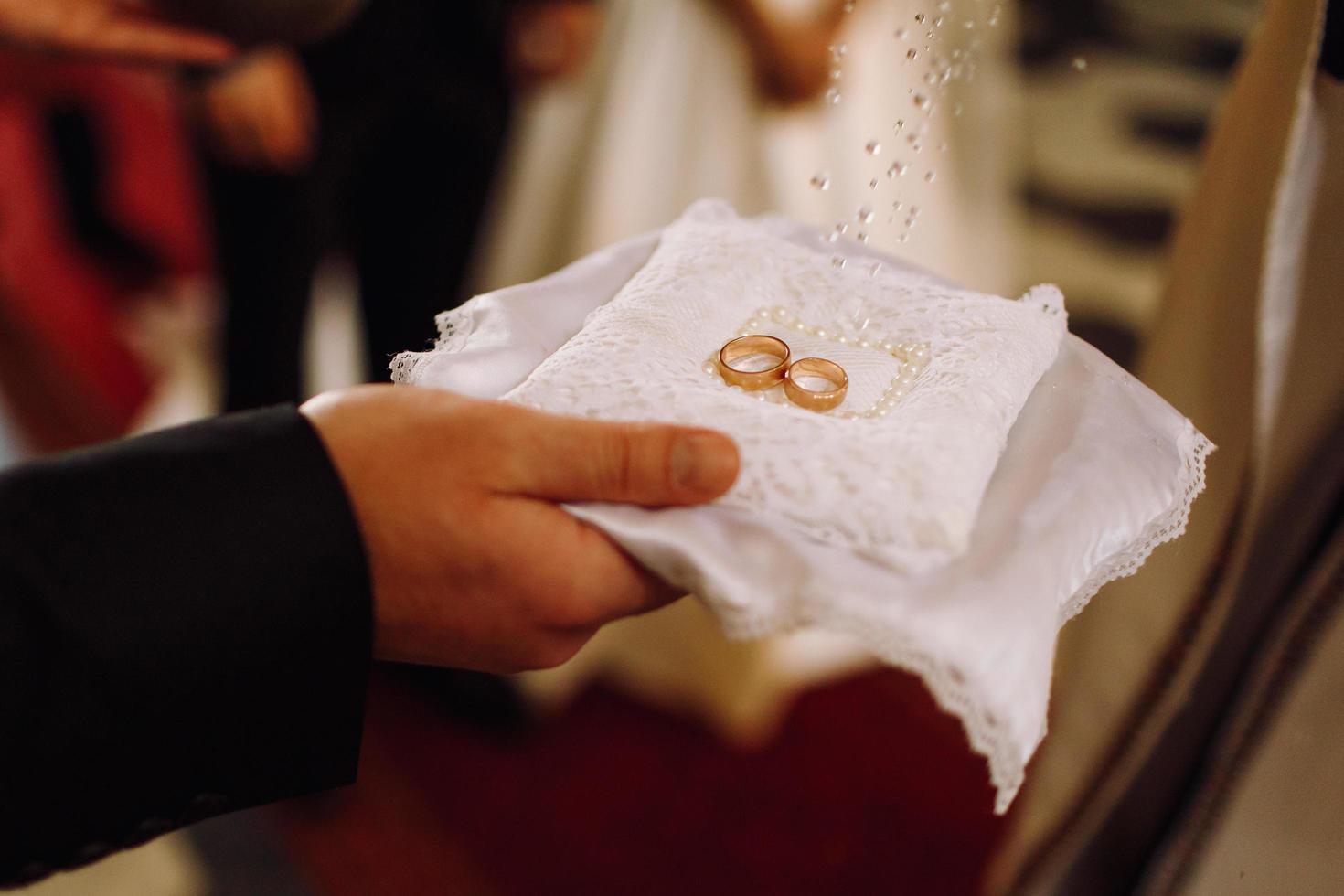 Groom holds golden wedding rings while priest blesses them photo