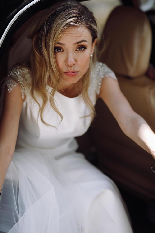 Blonde bride grimaces stepping out of black retro car photo