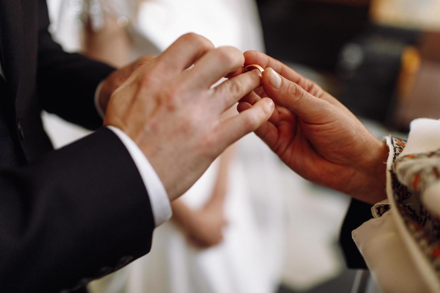 sacerdote pone el anillo de bodas en la mano del novio foto