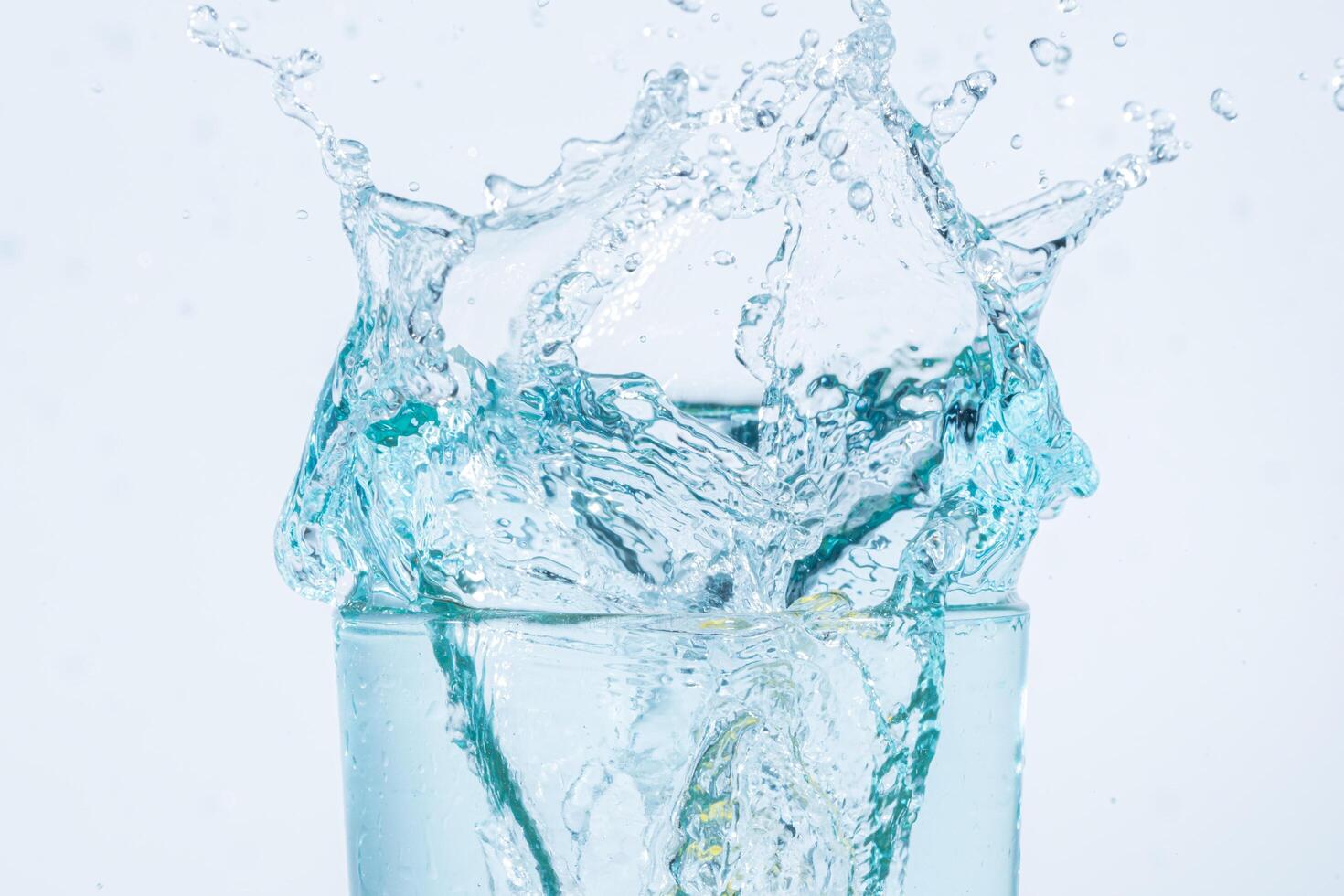 Salpicaduras de agua en un vaso sobre fondo blanco. foto