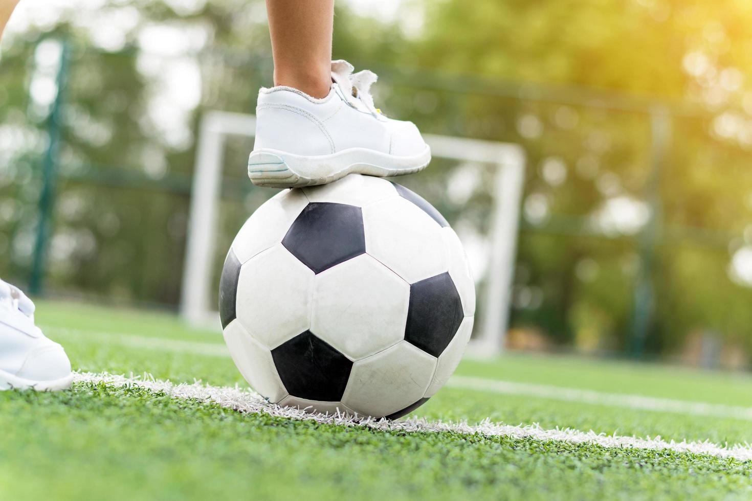 Pies de un niño vestido con zapatillas blancas pisando una pelota de fútbol foto