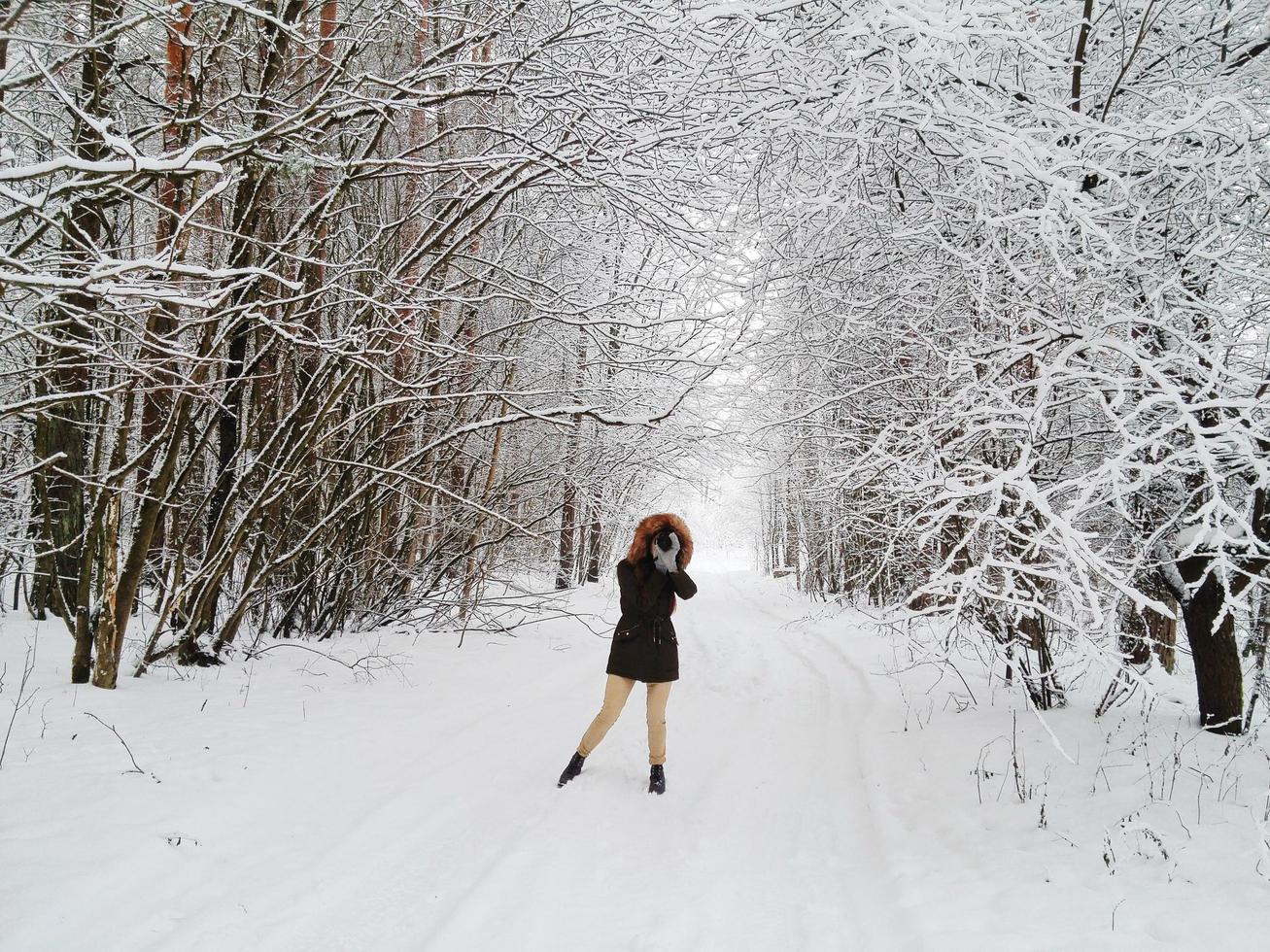 Latvia, 2020 - Woman in a black parka taking a photo in a snowy landscape
