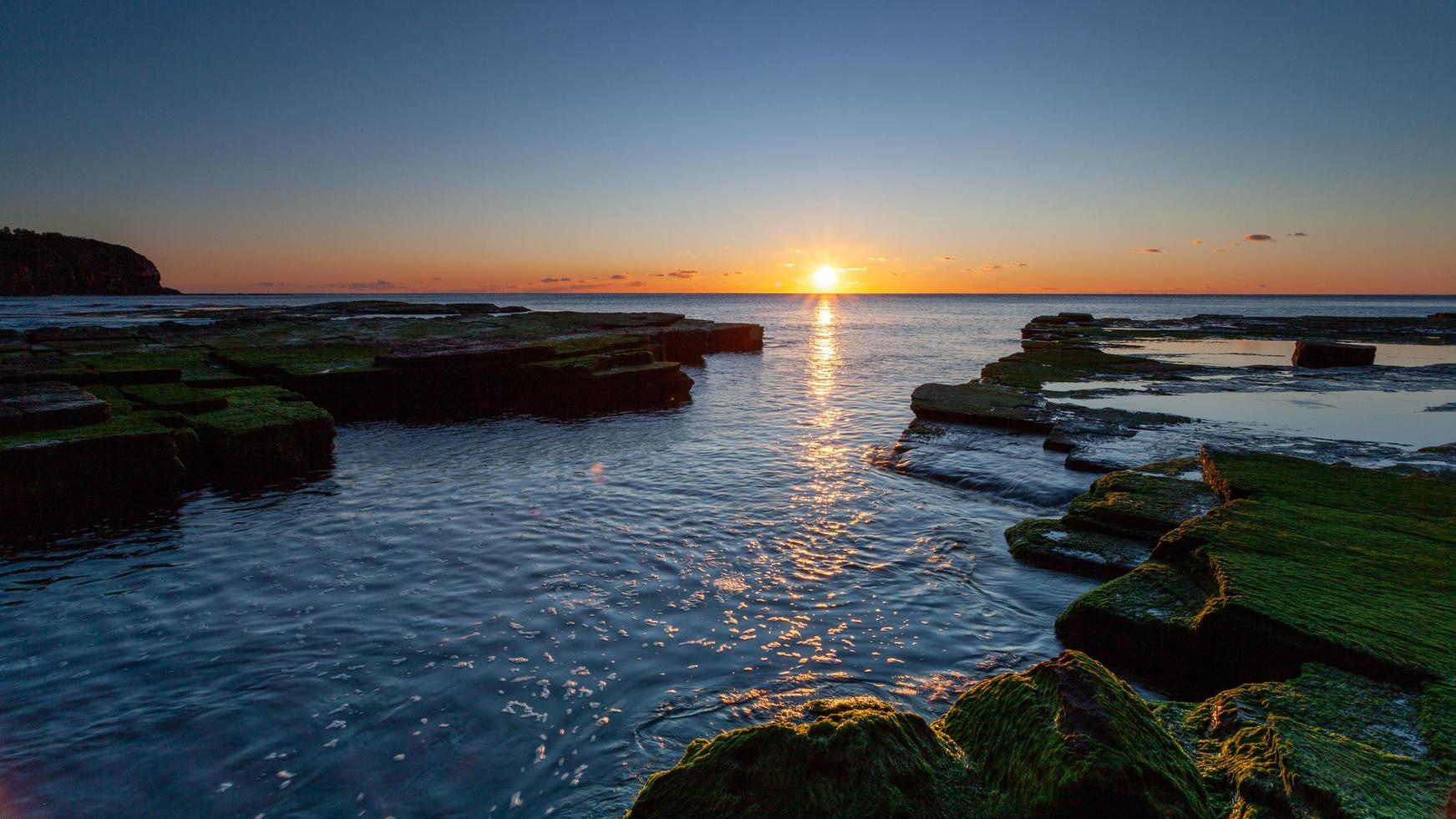 Rocas cubiertas de musgo cerca de la desembocadura del océano durante la puesta de sol foto